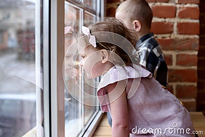 Children or siblings concept. Little girl and boy sitting at window and watching outside Stock Photo