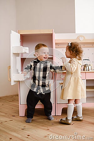 Children or siblings concept. Sweet toddler girl and boy playing with toy kitchen in light room Stock Photo