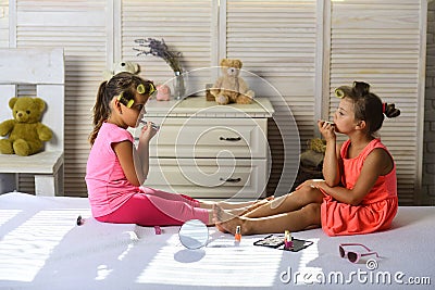 Children sit on bed with lipstick, nail polish and mirror Stock Photo