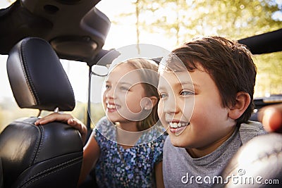 Children Sitting In Back Seat Of Open Top Car On Road Trip Stock Photo