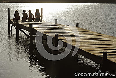 Children Sitting On Edge Of Jetty At Lake Stock Photo