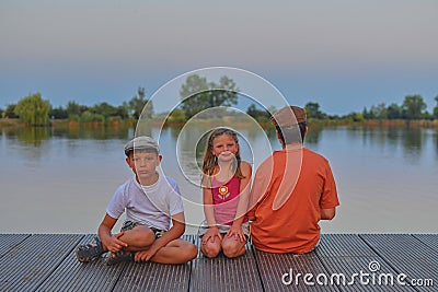 Children sitting on pier. Siblings. Three children of different age - teenager boy, elementary age boy and preschool girl sitting Stock Photo