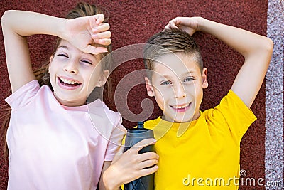 Children sport lifestyle theme. Happy boy and girl teenagers lie joyfully on rubber cover of running track of stadium Stock Photo