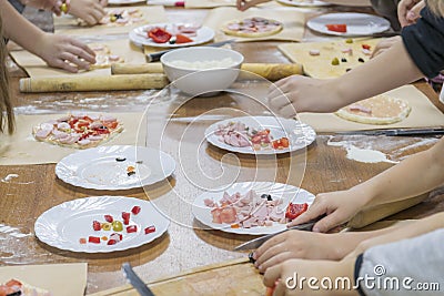 Children`s hands are cutting food for making their first pizza on wooden table. Cooking master class Stock Photo
