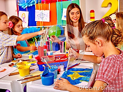 Children with teacher woman painting on paper in kindergarten . Stock Photo