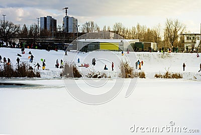 Children and their parents sledding from a snow slide in a city park with a frozen lake in Kiev Ukraine Stock Photo