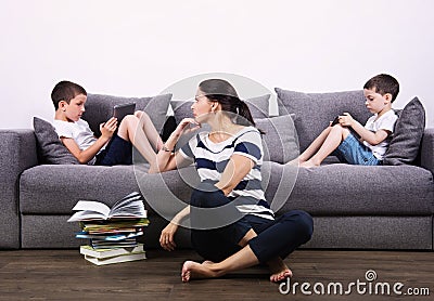 Children watch the tablets and their mother tries to read them book. Stock Photo