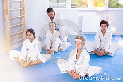 Children in white kimono sits in butterfly pose and practices stretching in sport gym Stock Photo