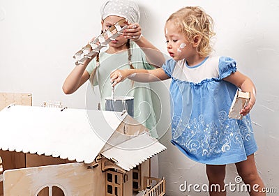 Children at work: Two girls sisters paint the roof of the doll house in white. The youngest girl intently makes smears Stock Photo