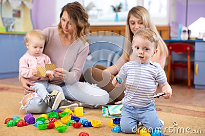 Children 1 year age playing in kindergarten or daycare centre under the supervision of moms Stock Photo