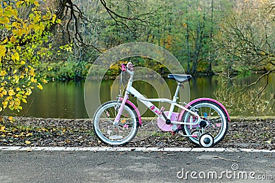 Childrens girls bicycle stands on path near pond at park under trees on autumn natural background Stock Photo