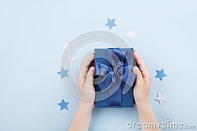 Childrens hands holding a gift or present box decorated confetti stars on blue table top view. Stock Photo