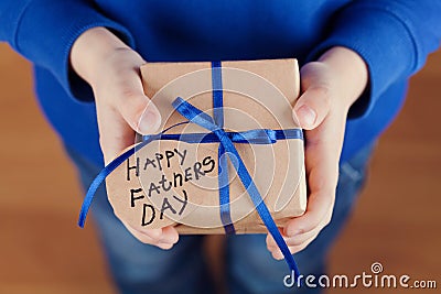 Childrens hands holding a gift or present box with kraft paper and tied blue ribbon tag on Happy fathers day Stock Photo