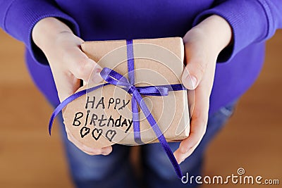 Childrens hands holding a gift or present in kraft paper and tag with note Happy Birthday, top view Stock Photo