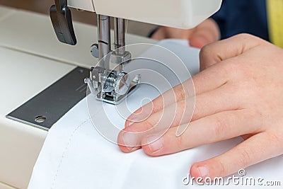 A childs hand pulling a white textil throught a sewing machine Stock Photo