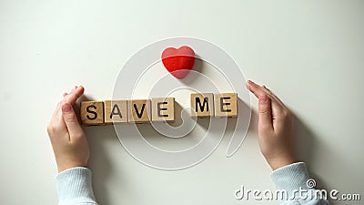 Childs hand putting heart sign and save me phrase made of wooden cubes, charity Stock Photo