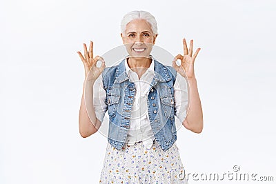 Chill, unbothered happy old woman with grey haircut, wear denim vest, dress, showing everything okay, ok gesture Stock Photo