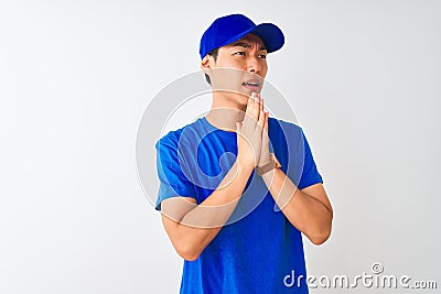 Chinese deliveryman wearing blue t-shirt and cap standing over isolated white background begging and praying with hands together Stock Photo