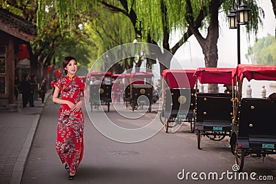 Chinese lady in red cheongsam dress walking near a Tourists riding Beijing traditional rickshaw Stock Photo