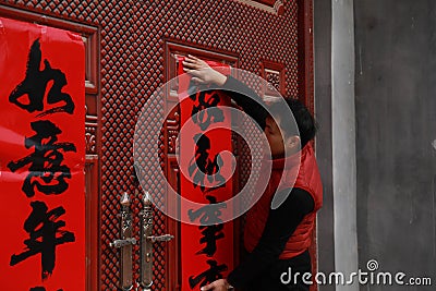 Chinese man post new year`s scrolls , Spring festival couplets and Mars at red door in China Stock Photo