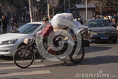 Chinese man riding a cargo tricycle loaded with goods in a street in Beijing, China. Cargo bikes or freight tricycles are popular Editorial Stock Photo