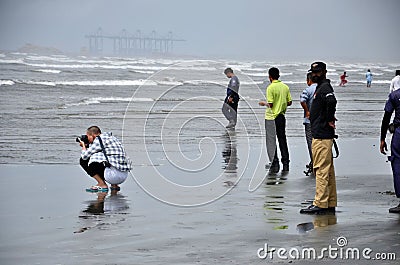 Chinese man squats with camera taking photo at Sea View beach water Karachi Pakistan Editorial Stock Photo