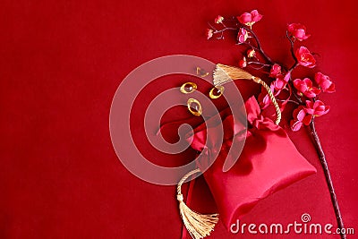 Chinese New Year, blooming plum blossom flower branch with red silk pocket money bag and gold ingot on red background, lucky item Stock Photo