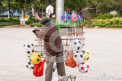 A chinese senior male street vendor selling a variety of toys in the public garden of Nansa, Yunnan, South China Editorial Stock Photo