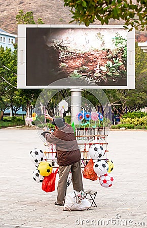 A chinese senior male street vendor selling a variety of toys in the public garden of Nansa, Yunnan, South China Editorial Stock Photo