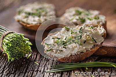 Chive cream cheese spread on a bread slices next to bunch of freshly cut chives on a rustic wood and chopping board Stock Photo