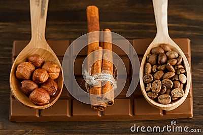 Chocolate bar, shelled hazelnuts, roasted coffee beans, cinnamon on wooden background Stock Photo