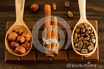 Chocolate bar, shelled hazelnuts, roasted coffee beans, cinnamon on wooden background Stock Photo