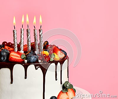 Chocolate Birthday sweet cake with fresh fruits, berries and lighted candles on top over a popular light pink Stock Photo