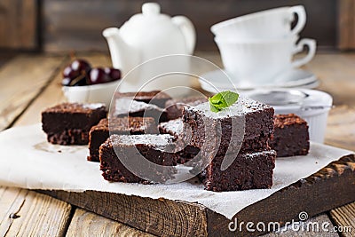 Chocolate brownies with powdered sugar and cherries on a dark wooden background. Stock Photo