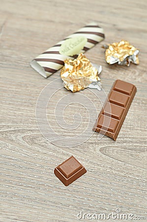 A chocolate candy bar with a piece broken off with the wrappers out of focus Stock Photo