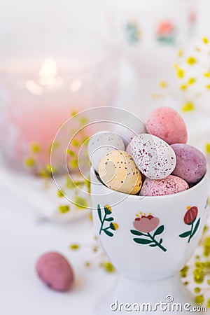 Chocolate candy colored Easter eggs in ceramic cup burning candle, small flowers Stock Photo