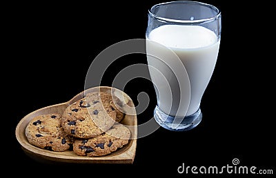 Chocolate chip cookies on a heart shaped plate with a glass of fresh milk on black background Stock Photo