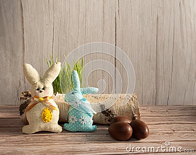 Chocolate eggs, funny handmade textile Easter bunnies and grass on a light wooden background. Stock Photo