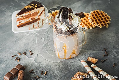 Chocolate milkshake with dripping sauce, cream, cookies and cake on dark table Stock Photo