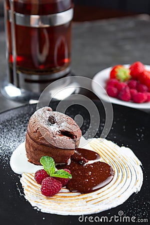 Chocolate pudding lava cake with vanilla cream, raspberry and mint on a black plate Stock Photo