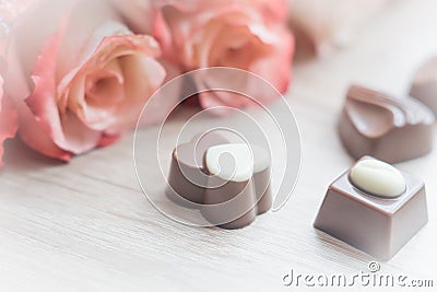 Chocolate sweets and pale roses on wooden table, toned Stock Photo
