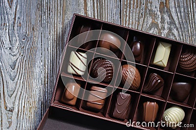 Chocolates in different shapes and colors in gift box on wooden table. Flat lay. Stock Photo