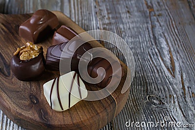 Chocolates in different shapes and colors over rustic wooden board. Stock Photo