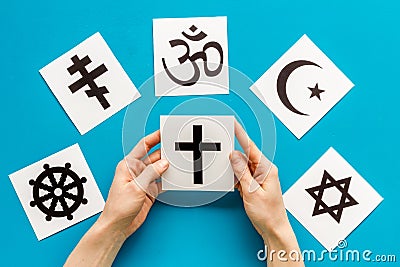 Choose religion concept. Hand with catholic cross near world religions symbols on blue background top view Stock Photo