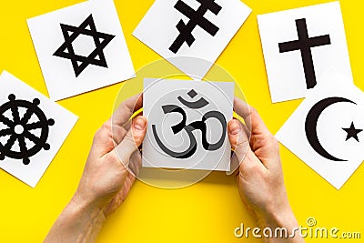 Choose religion concept. Hands with Buddhist Om sign near world religions symbols on yellow background top view Stock Photo