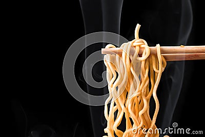 Chopsticks pick up tasty noodles with smoke on dark background. Stock Photo