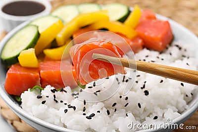 Chopsticks with salmon over delicious poke bowl , closeup Stock Photo