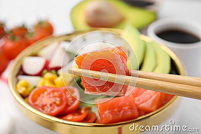 Chopsticks with salmon over delicious poke bowl, closeup Stock Photo