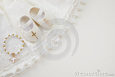 Christening background with baptism baby dress, shoes, and cross on pastel background Stock Photo