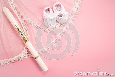 Christening background with baptism baby shoes, dress and candle on pink background. Stock Photo